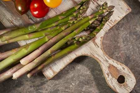 Fresh green asparagus and tomatoes on wooden cutting board, closeupの写真素材