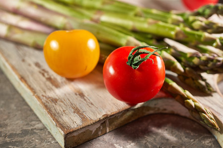 Fresh asparagus and cherry tomatoes on wooden board, closeupの写真素材