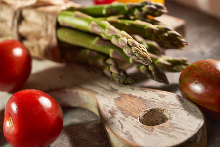 Fresh asparagus and tomatoes on wooden cutting board, closeupの写真素材