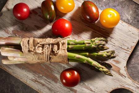 Bunch of asparagus and tomatoes on wooden cutting board.の写真素材