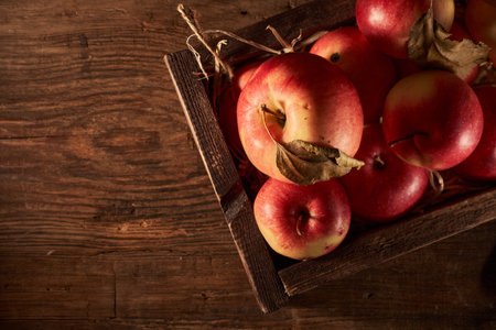 Ripe red apples in a wooden box on a wooden background.
