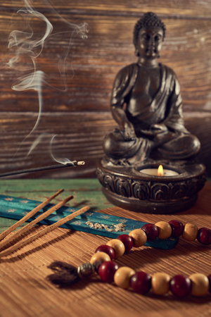 Buddha statue and incense sticks on a wooden background.の写真素材