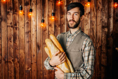 Man baker with baguettes on a wooden retro background. Hipster beard.の写真素材