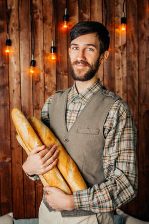 Man baker with baguettes on a wooden retro background. Hipster beard.の写真素材