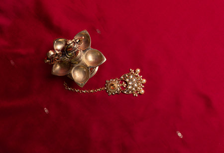Indian traditional bronze oil lamp in the shape of a bird and gold Indian female jewelry on the red sari background. traditional Indian religious ceremony of Hindusの写真素材