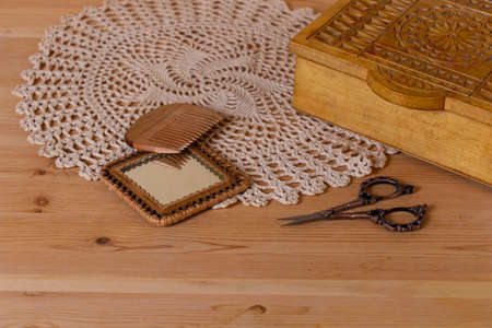Women's dressing table in retro, vintage style. A box, a mirror, a comb, scissors, a knitted napkin on the background of a natural wooden tableの写真素材