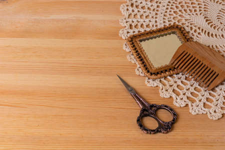 Women's dressing table in retro, vintage style. A mirror, a comb, scissors, a knitted napkin on the background of a natural wooden tableの写真素材
