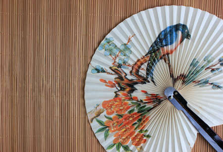 chinese fan with a bird pattern on bamboo mat background. still life.の写真素材