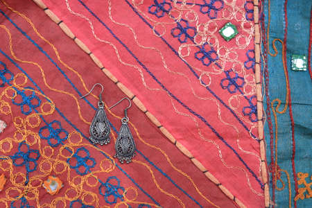 Indian silver earrings on the background of a traditional patchwork carpet. Indian background