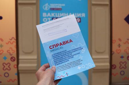 Moscow. Russia. December 8, 2021. The hand holds a new real certificate of vaccination in the shopping center. "GUM" Text in Russian: "Certificate of vaccination against a new coronavirus infection (covid 19)"のeditorial素材