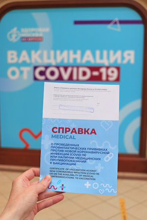 Moscow. Russia. December 8, 2021. The hand holds a new real certificate of vaccination in the shopping center. "GUM" Text in Russian: "Certificate of vaccination against a new coronavirus infection (covid 19)"のeditorial素材