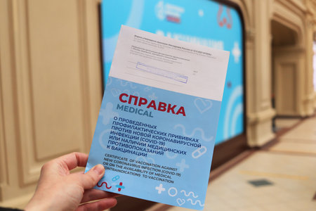 Moscow. Russia. December 8, 2021. The hand holds a new real certificate of vaccination in the shopping center. "GUM" Text in Russian: "Certificate of vaccination against a new coronavirus infection (covid 19)"のeditorial素材
