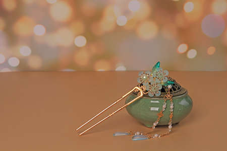Still life in Chinese style. Green incense box and hairpin with jade flower on beige background