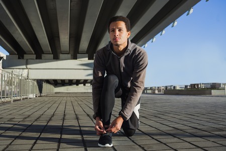 Portrait of fit young black guy tying shoe laces before a runの写真素材