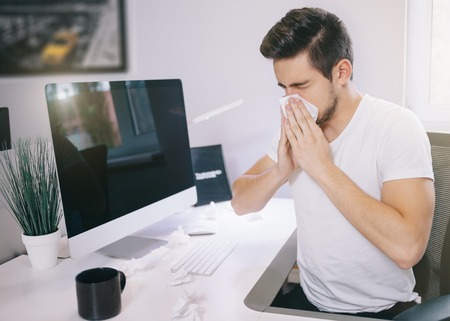 Side view of the patient's employer. sneezing into a tissue in an office near the window in the computer. Freelancer designer with a cold