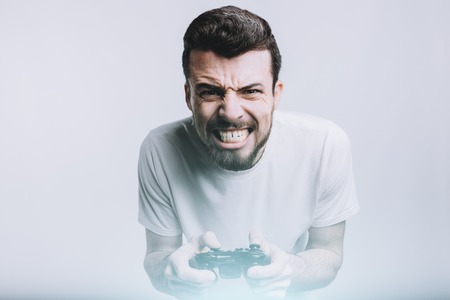 Young stylish man with beard holding joystick and trying to win this hard game battle. He is really concentrated and serious. Isolated on white backgroundの写真素材