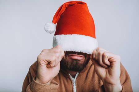 Young handsome man with noel or santa hat. Comic funny man has pulled on his red hat with both hand. Isolated on white backgroundの写真素材