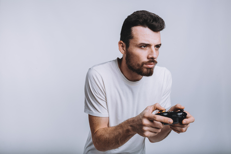 Young attractive guy with beard holding joystick. Funny man is really concenrated on serious game. He is going to win that tough battle. Isolated on white backgroundの写真素材