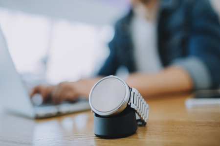 Man working on a laptop in cafe. Young freelancer is sitting in cafeteria and typing on macbook. He has a nice watch on the table, that is in focus. Close up. Place for your logo or ad.の写真素材