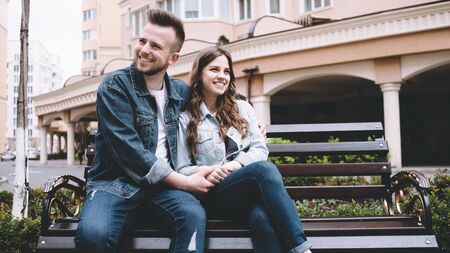 Attractive young couple in love resting on the bench outside holding each other with hands. They are smiling for having such a wonderful dayの写真素材