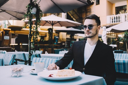 Stylish and confident businessman is sitting at the table outside. He hasnt started to eat his tasty lunch yet. The guy is looking straight forward with his glasses on. Close upの写真素材