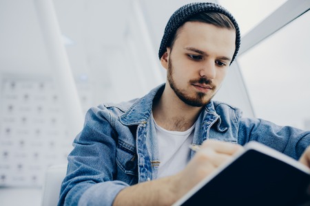 Smiling man is sitting on sofa and writing in his his noteook. He is busy working guy