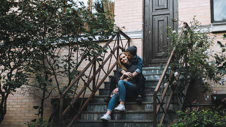 A picture of boy and girl sitting together at stairs near a beautiful building. He is embracing her...