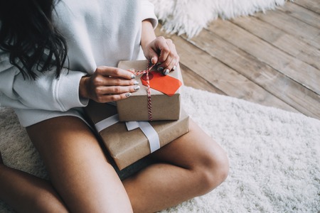 Close up of Christmas boxes full of interesting presents. It is prepared for family of a girl that holds them on knees. There are two gifts. One of them is big while the other one is small. She wants to give it to her parents. Close up. Cut viewの写真素材
