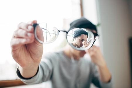 Close up of stylish glasses that the hipster is holding. The guy is tired so thats why he is rubbing his eyesの写真素材