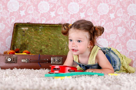 Little girl playing on his stomach, situated near the suitcase with toys