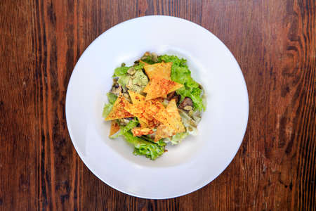 in a plate on a table is salad with chips, iceberg lettuce, mushrooms, pumpkin seeds. top viewの写真素材