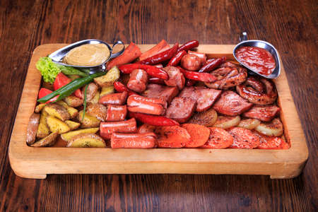 on the table is a wooden board. on board - Assorted fried sausages, grilled carrots, onions HaGelilit, grilled potatoes, sauce Adjika, Mustard Sauceの写真素材
