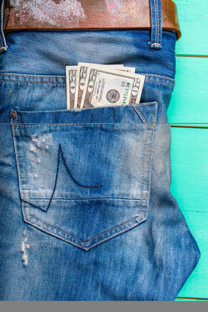 $ 20 bill in the pocket of jeans, jeans neatly stacked on wooden background, top viewの写真素材