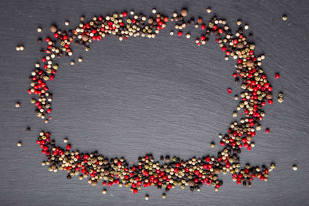 colored peppers scattered  on a circle on the slate board. top view. a place for an inscription.の写真素材