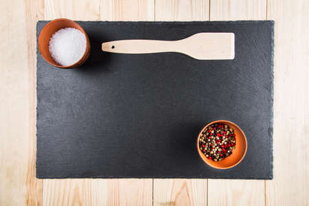 multicolored peppers peas and salt in a clay cup on a slate board, wooden kitchen spatula, top viewの写真素材