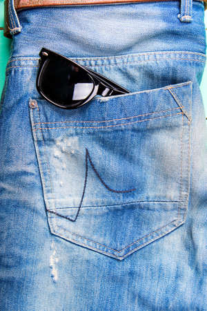 sunglasses in the pocket of jeans, jeans neatly stacked on wooden background, top viewの写真素材