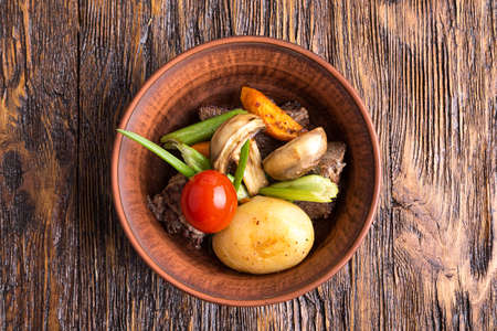 stew with vegetables in an earthenware dish. mushrooms, carrots, tomatoes, celery, onions. top view