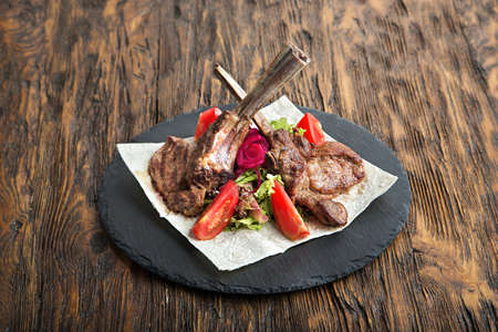 ribeye steak on the bone, tomahawk, served with tomatoes and iceberg lettuce on pita on slate board.