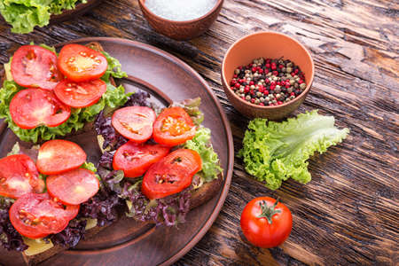Three sandwiches with fresh tomato and lettuce on a clay plate. Nearby are spices - salt and pepper.の写真素材