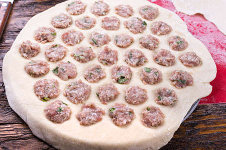 Prepare raw homemade food - dumpling in metal strainer pelmennica. They have a traditional form. Pork, chicken mincemeat. Background is red.の写真素材