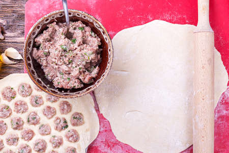 Prepare raw homemade food - dumpling in metal strainer pelmennica. They have a traditional form. Pork, chicken mincemeat. Background is red.の写真素材