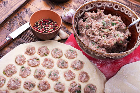 Prepare raw homemade food - dumpling in metal strainer pelmennica. They have a traditional form. Pork, chicken mincemeat. Background is red.の写真素材