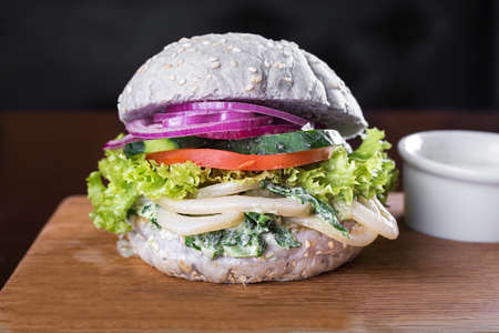 blue burger with fried squid and creamy spinach sauce on a wooden boardの写真素材