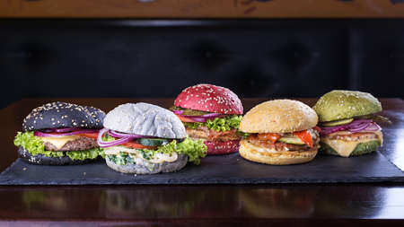 Assorted colored burgers with different fillings, with sesame seeds on slate blackboardの写真素材