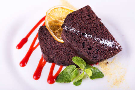 piece of chocolate cake on a plate, decorated with berry topping, mint and slice of lemonの写真素材