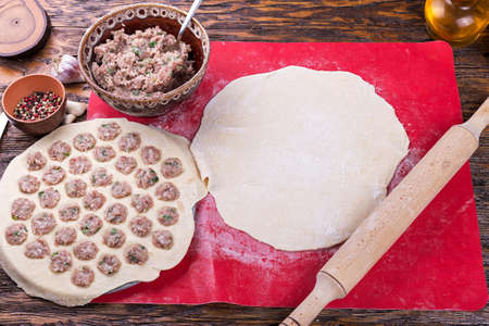 Prepare raw homemade food - dumpling in metal strainer pelmennica. They have a traditional form. Pork, chicken mincemeat. Background is red.の写真素材