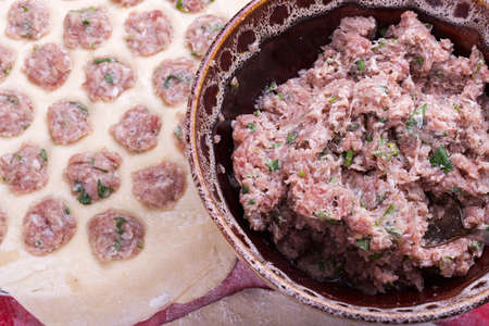 Prepare raw homemade food - dumpling in metal strainer pelmennica. They have a traditional form. Pork, chicken mincemeat. Background is red.の写真素材