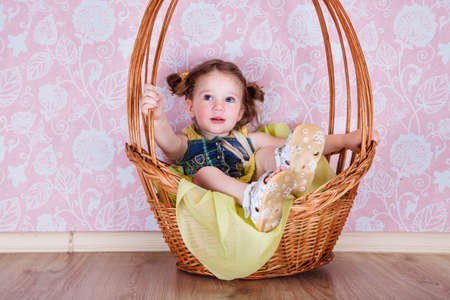 little cute girl sitting on a wicker basket, a photo shoot in the studioの写真素材