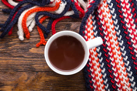 hot cocoa in a cup on a wooden background, next to the cup is warm scarfの写真素材