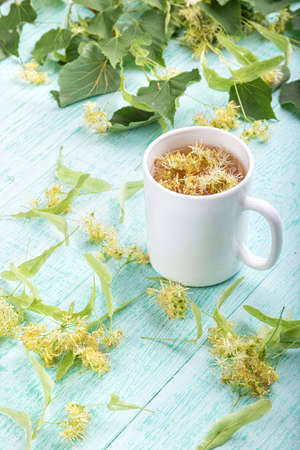 Lime brewed tea in a cup on a wooden table. on a table scattered linden blossoms and leavesの写真素材